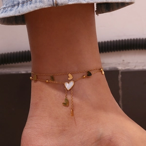 Detail shot of double-layer gold heart anklet with white shell heart and tassel accents