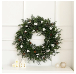 Close-up of cedar Christmas wreath with pine cones and faux snow on a white wall
