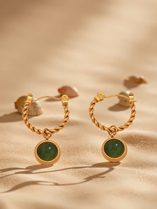 Macro view of gold twisted hoop earrings with green agate pendants on beach sand
