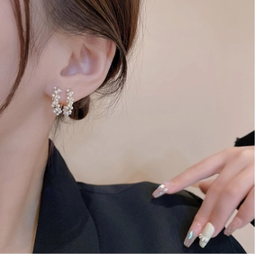 Close-up of elegant geometric pearl earrings with gold metal frame worn by a model