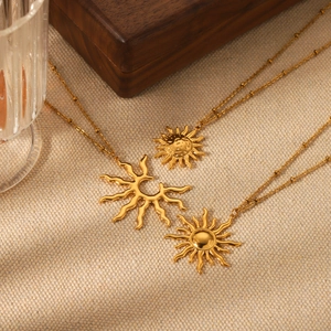 Three gold stainless steel sun pendant necklaces on elegant beige textured fabric background