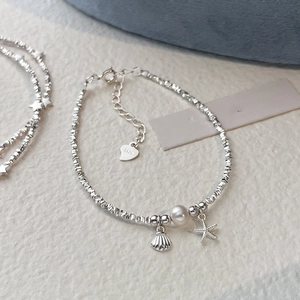 Silver starfish and shell charm bracelet with a white pearl on a textured background