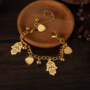 Polished gold Hamsa Hand and heart charm bracelet on a minimalist wooden tray display
