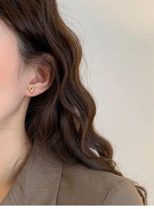 Close-up of minimalist gold V-shaped stud earring worn on ear with polished finish