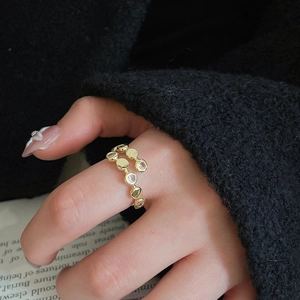 Detail of a layered golden ring with zircons worn by a model on a minimalist background