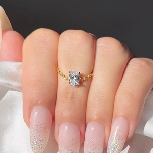 Macro shot of an oval white zircon ring with gold plated chain on white silk fabric