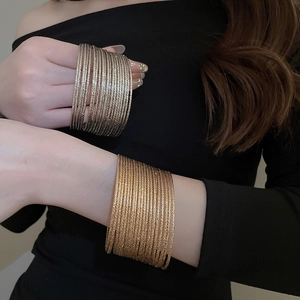 Detail of stacked gold and silver textured metal bangles worn on a model's wrist