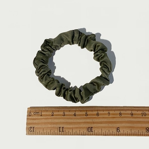 Detailed view of an olive green silk satin hair scrunchie showing 5.5cm size on a ruler