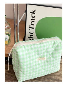 Détail d'une trousse à maquillage matelassée vert clair à carreaux sur bois