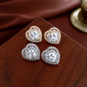 Macro shot of gold and silver heart-shaped stud earrings with sparkling zircon halos