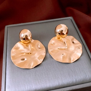 Detailed macro view of gold ball stud and irregular hammered metal disc earring