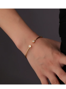 Close-up of a gold open bangle featuring two sparkling round zircons on a woman wrist