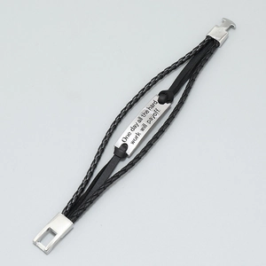 Detail of multi-layer black woven leather bracelet with engraved silver metal bar plate