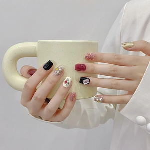 Handmade cat-eye press-on nails with dark red and gold glitter designs on white suit model