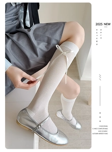 Detail of white ribbed knee-high socks with delicate bow accents and silver Mary Jane shoes