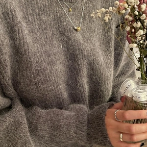 Detail of layered round bead necklaces and rings paired with a grey fuzzy knit sweater