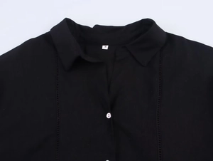 Detail of black linen shirt showing V-neck, white buttons and hollow-out lace stitching