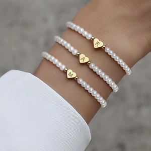 Close-up of three pearl bracelets featuring gold heart charms with letters R, A, and M