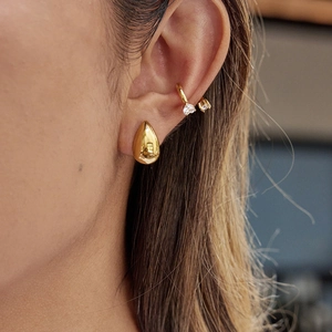 Détail d'une boucle d'oreille goutte d'or et d'un faux piercing serti de zircon