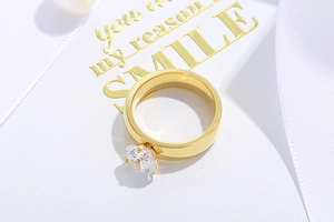 Detail view of a gold heart-shaped zircon ring on a white ribbon and decorative card