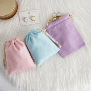 Three pastel cotton drawstring jewelry pouches in pink, blue, and purple on white fur