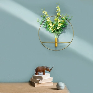 Detail of round golden metal wall wreath with yellow and green faux flowers on teal wall