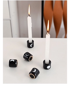 Close-up of black ceramic candle holders with white moon patterns and lit tall candles