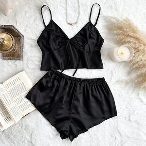 Two-piece black satin lingerie set with V-neck camisole and shorts on plush background