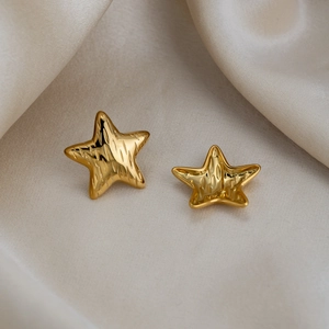 Macro detail of star-shaped golden earrings with textured surface on silk background