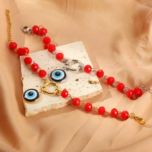 Detail of red crystal beaded bracelet with evil eye charms on light gold silk and stone