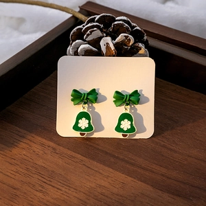 Detail of festive green bow earrings with bell pendants and white snowflake patterns