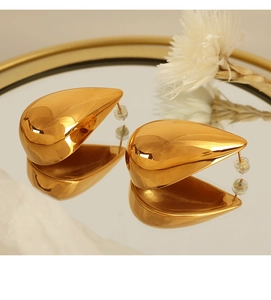 Close-up of golden teardrop earrings with mirror finish reflecting on a gold tray
