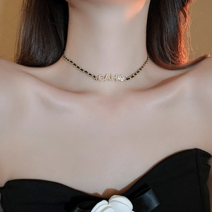 Detail of gold-plated choker necklace with camellia flower and rhinestone initials