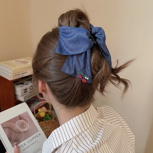 Blue denim bow hair claw clip with embroidered cherries and pearls on model hair