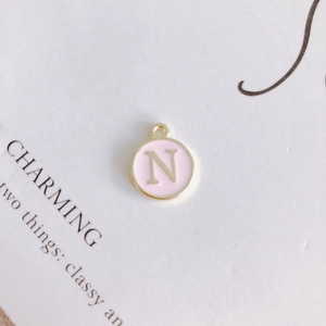 Macro detail of round pink enamel letter N pendant with gold metal trim for DIY jewelry