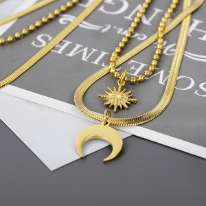 Macro detail of gold layered necklace featuring sun and moon pendants on snake and bead chains