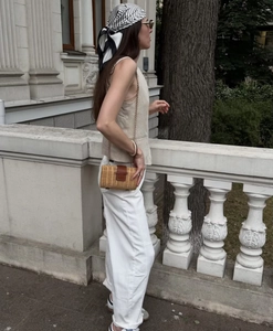 Detail of a beige linen vest and white casual pants with a straw crossbody chain bag