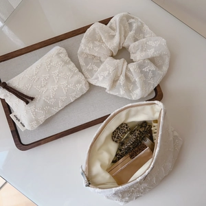 Detailed close-up of lace embroidery makeup bags and floral scrunchie on wood tray