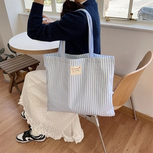 Close-up of a blue and white striped canvas tote bag in a sunlit lifestyle cafe setting