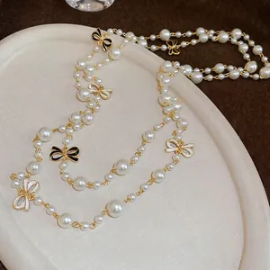 Elegant long pearl necklace with black and white enamel bows on a white display tray