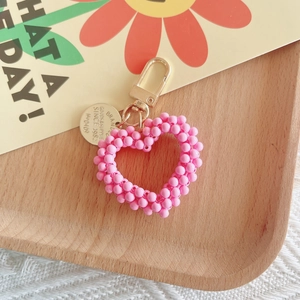 Detail view of a handmade pink pearl heart keychain with golden clasp on a wooden tray