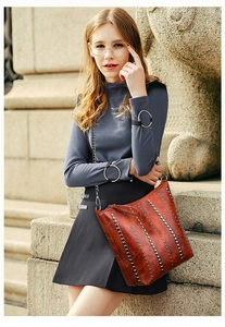Detail of red-brown PU leather shoulder bag with metal studs and chain strap on model