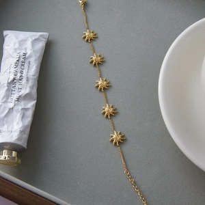 Dettaglio di un bracciale dorato con cinque ciondoli a forma di girasole su vassoio grigio
