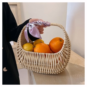 Close-up of a woven straw basket bag with a pink silk scarf and fresh citrus fruits