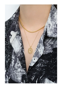 Detail of layered gold beaded necklace and tulip pendant on a model in floral shirt