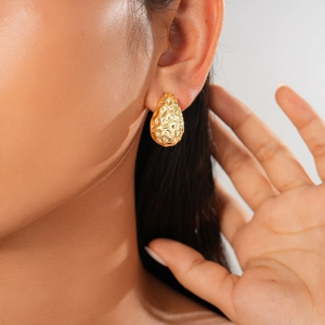 Close-up of gold drop earrings with hammered texture on a model showing refined metal detail