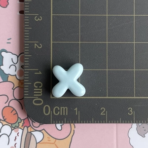 Macro view of a 1cm mini light blue resin cross charm on a measuring scale mat