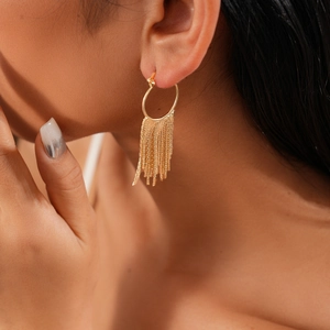 Close-up of a gold hoop earring with long metallic chain tassels worn by a model