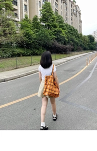 Lifestyle shot of an orange plaid tote bag worn by a model in a casual city setting
