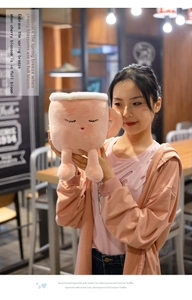 Detail of pink latte cup plush toy with cute closed-eye embroidery held in a warm setting